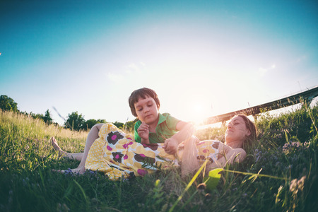 The boy and his mother are lying in the meadow. A woman and her son are walking in the field in the setting sun. The kid spends time with mom on the nature. Mom's smile. A child is hugging mother.の写真素材