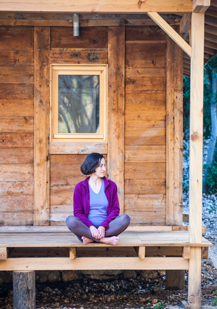A woman is sitting on the porch of an old wooden house. Barefoot girl resting near the house on a warm spring day.の写真素材