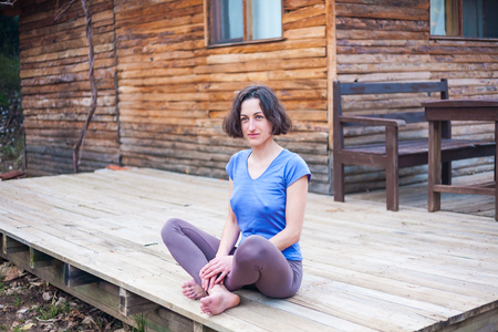 A woman is sitting on the porch of an old wooden house. Barefoot girl resting near the house on a warm spring day.の写真素材