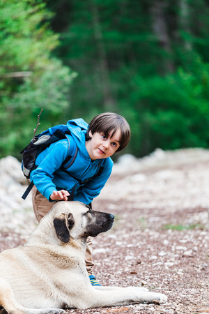 A boy with a backpack walks with the dog through the park. The child is petting the dog. Shepherd goes with its owner in the woods. Friendship pet and child.の写真素材