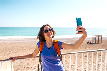 A girl takes a selfie on the waterfront. A woman walks through the resort town and takes pictures. Brunette travels around the Turkish city. Photo on the background of the sea.の写真素材