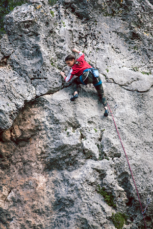 A girl climbs a rock. The athlete trains in nature. Woman overcomes difficult climbing route. Strong climber. Extreme hobby.の写真素材