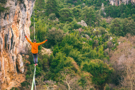 A man is walking along a stretched sling. Highline in the mountains. Man catches balance....
