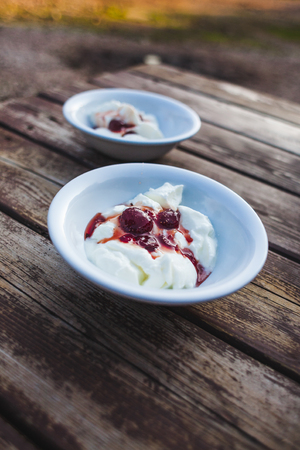 Ice cream with strawberry jam. Two bowls of yogurt on a wooden table. Creamy ice cream with berry syrup.の写真素材