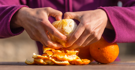 Oranges in female hands close up. Peeled citrus fruits. Woman peels oranges from peel.の写真素材