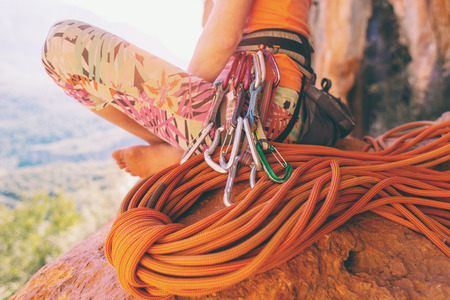 Climber sits near the rope and prepares to overcome the route. Slender girl holds climbing equipment. A woman on the background of beautiful mountains. Rest after climbing.の写真素材