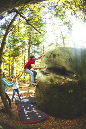 Bouldering in nature. Climbing on natural terrain. Safety in rock climbing. Friends train in nature. Active lifestyle. Teamwork. A man climbs on a big stone, and friends insure him.の写真素材