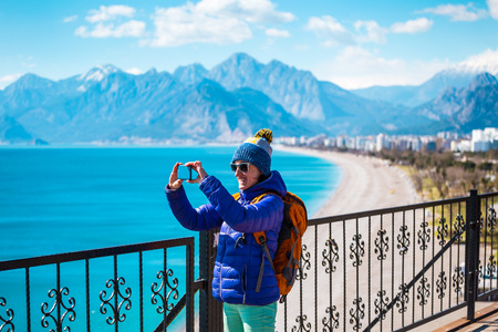 A girl takes a selfie on the waterfront. A woman walks through the resort town and takes pictures. Brunette travels around the Turkish city in winter. Photo on the background of the sea and mountains.の写真素材