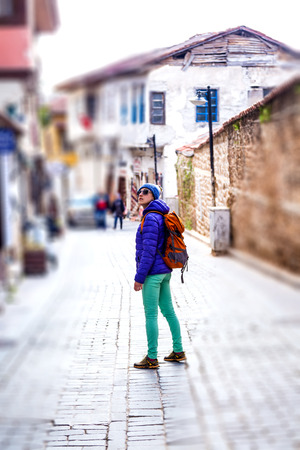 The girl visits the sights of the old Turkish city. A woman with a backpack is walking along the street of a resort town. A woman in a jacket and hat looks at old buildings. Travel to Turkey.の写真素材