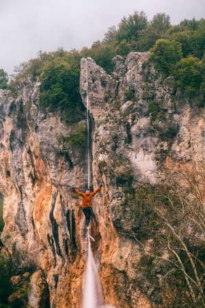 A man is walking along a stretched sling. Highline in the mountains. Man catches balance. Performance of a tightrope walker in nature. Highliner on the background of the mountains.の写真素材