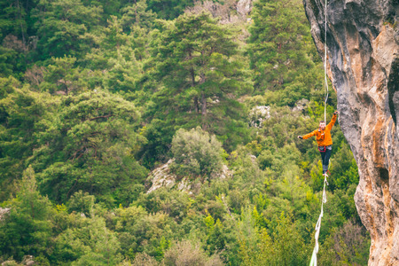 A man is walking along a stretched sling. Highline in the mountains. Man catches balance. Performance of a tightrope walker in nature. Highliner on the background of thunderclouds.の写真素材