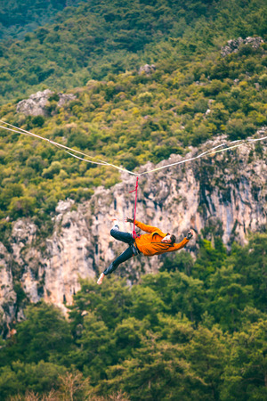 A man is walking along a stretched sling. Highline in the mountains. The man has lost balance. Performance of a tightrope walker in nature. Highliner hanging on a rope. Fall athlete.の写真素材