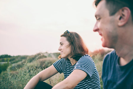A company of friends is resting in nature. Man and woman are sitting in the field at sunset. A...