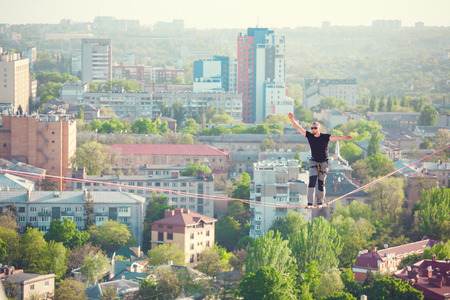 A man walks along a line stretched between two buildings. Extreme entertainment. Fear of heights. The man is balancing over the city.の写真素材