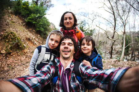 The family takes a selfie in nature. Travel with children. The boy travels with his brother and parents. Walk along the mountain path. Active lifestyle. Tourists with backpacks in the forest.の写真素材