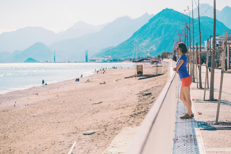 A girl walks along the new quay of Antalya. Woman looks at the Mediterranean. Brunette on the background of the Turkish mountains. Walk along the waterfront street. Holidays in Turkey.の写真素材