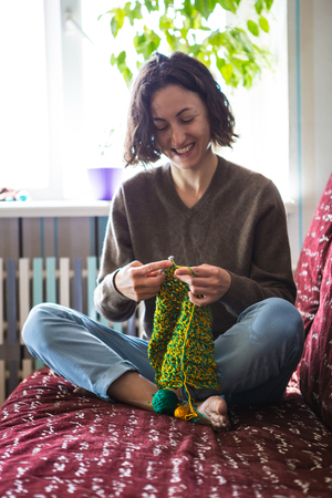 A woman knits from thick yarn. Handmade clothes. The girl sits on the couch and goes in for her hobbies. Knitting close up.の写真素材