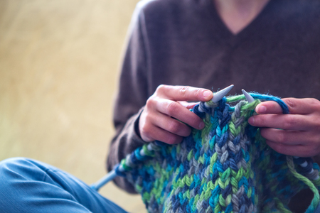 A woman knits from thick yarn. Handmade clothes. The girl sits on the couch and goes in for her hobbies. Knitting close up.の写真素材