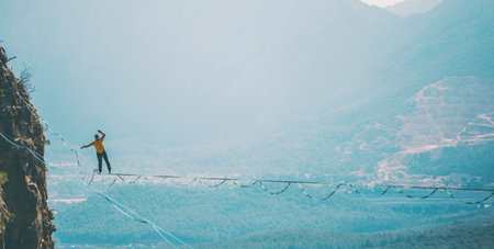 A man is walking along a stretched sling. Highline in the mountains. Man catches balance....