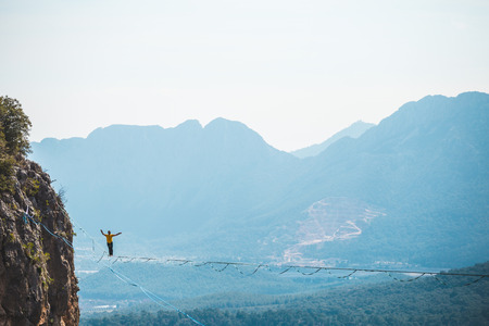 A man is walking along a stretched sling. Highline in the mountains. Man catches balance. Performance of a tightrope walker in nature. Highliner on the background of the mountains.の写真素材