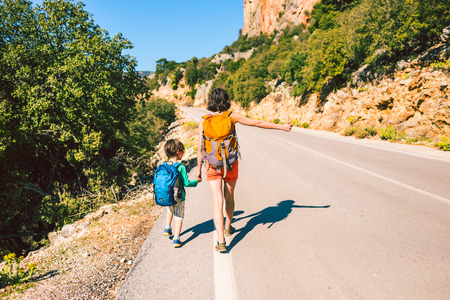 Woman with a child hitchhiking. The girl catches the car. Brunette with a backpack and young son waiting for transport. Hitchhiking in Turkey. The boy with his mother stands on a mountain road.の写真素材