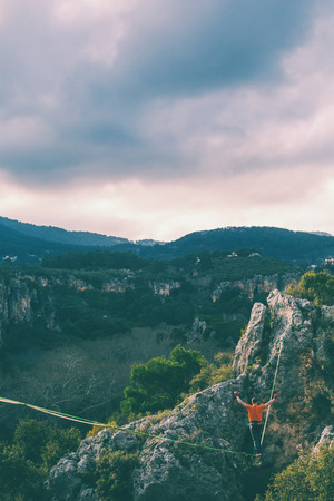 Highline in the mountains. A man walks along a stretched sling against a cloudy sky. Highline is on the line. Ropewalker catches the balance. Equilibrium.の写真素材