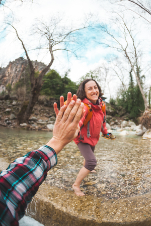 Girl greets friend. A woman with a friend is walking in the woods. The couple travels to scenic places. The girl gives five. Gesture of greeting. A tourist crosses a mountain river to a ford.の写真素材