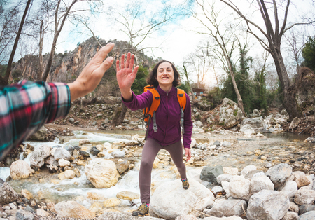 Girl greets friend. A woman with a friend is walking in the woods. The couple travels to scenic places. The girl gives five. Gesture of greeting. A tourist crosses a mountain river to a ford.の写真素材