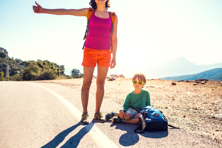 Woman with a child hitchhiking. The girl catches the car. Brunette with a backpack and young son waiting for transport. Hitchhiking in Turkey. The boy with his mother stands on a mountain road.の写真素材