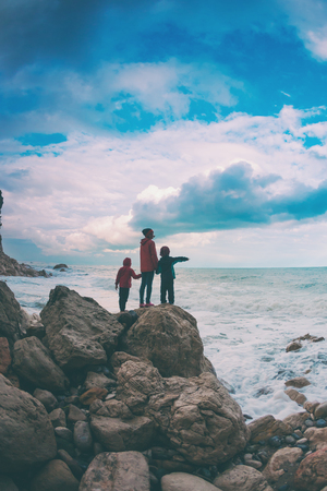 A woman with her son are standing on a stone and looking at the sea. The boy with his mother look at the waves. The child is walking along the ocean shore. Silhouette of mom and child against the sky.の写真素材