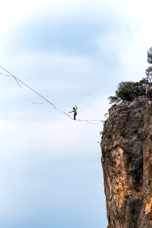 Highline on the background of the mountains makes a step. A man is walking along a stretched sling. Performance of a tightrope walker. Highliner balances over the abyss. Highline between two rocks.の写真素材