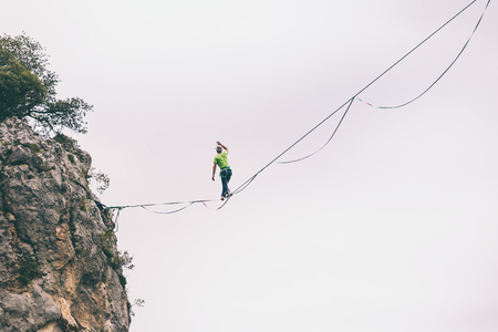 Highline on the background of the mountains makes a step. A man is walking along a stretched sling. Performance of a tightrope walker. Highliner balances over the abyss. Highline between two rocks.の写真素材
