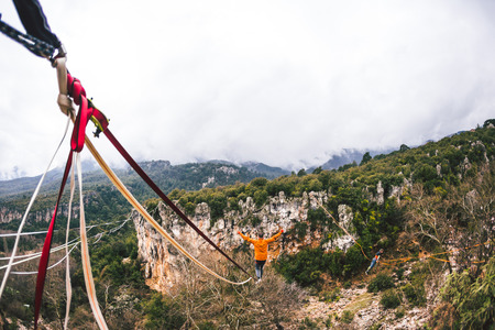 Highline in the mountains. A man walks along a stretched sling against a cloudy sky. Highline is on the line. Ropewalker catches the balance. Equilibrium.の写真素材