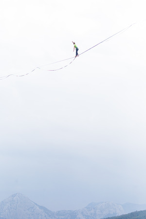Highline on the background of the mountains and cloudy sky. A man is walking along a stretched sling. Performance of a tightrope walker. Highliner balances over the abyss. Highline between two rocks.の写真素材
