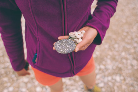 The girl collects sea stones and shells. Small pebbles in the female palm. Seashells in hand.