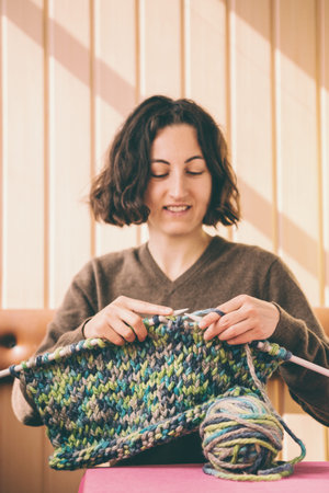 A woman knits from thick yarn. Handmade clothes. The girl sits on the couch and goes in for her...