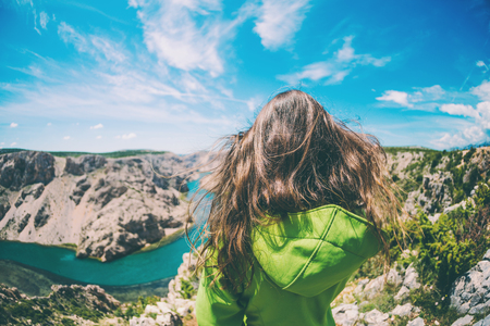 A girl with long hair growing in the wind stands on the edge of a canyon. Krka National Park. Bend of the river at the bottom of the canyon. A woman travels to picturesque places in Croatia.の写真素材