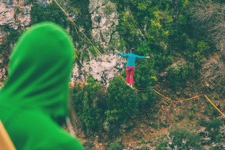 A woman is walking along a stretched sling. Highline in the mountains. Woman catches balance....