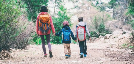 A woman with two children goes through the forest. The boy walks in the park with his mother and brother. Family holiday. Brunette with a backpack travels with children. Mom holds sons hands.の写真素材