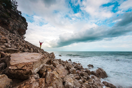 A man stands a huge stone against the sea and a beautiful sky. Traveler walks along the coast of the...