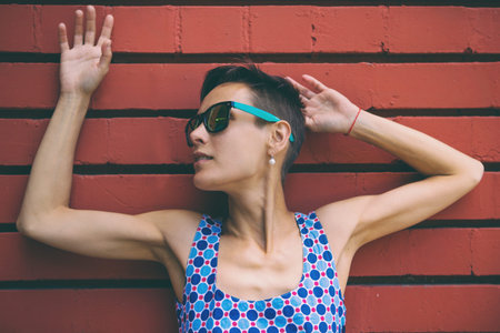 Woman against the background of a red brick wall. Brunette with glasses walks down the street. Girl...