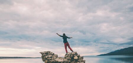 The girl stands on a pile of stones and looks at the sea. Woman resting on the sea coast. Tourist explores the sights of Croatia. Female silhouette against the sunset sky.の写真素材