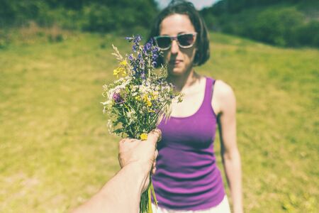 The man holds out a bouquet of wild flowers to the woman. A gift for a girl. The girl is standing in a meadow. Violet flowers in female hands. Date.の写真素材