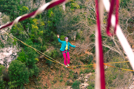 A woman is walking along a stretched sling. Highline in the mountains. Woman catches balance....