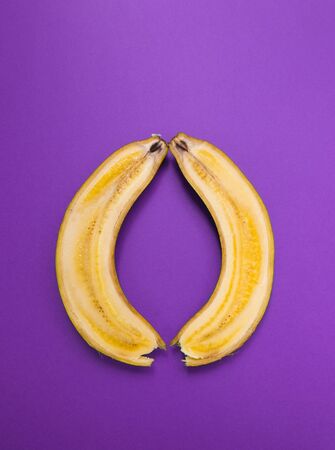Banana cut along. Two halves of a banana on a purple background. Ripe fruit.の写真素材