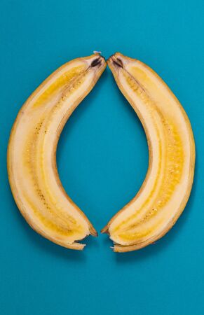 Banana cut along. Two halves of a banana on a blue background. Ripe fruit.の写真素材
