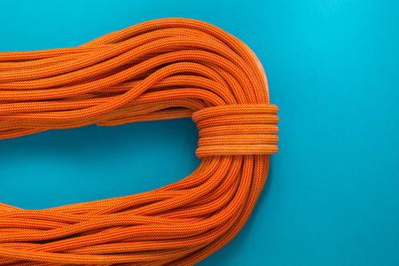 Bayed rope for climbing on a blue background. Orange rope for mountaineering close up. Node