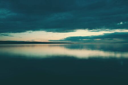 Night sky and sea. The setting sun and calm water. Sunset sky with clouds. Dark ocean water.の写真素材