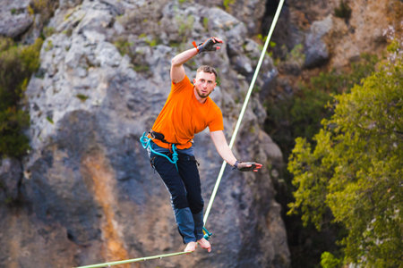 A man is walking along a stretched sling. Highline in the mountains. Man catches balance....