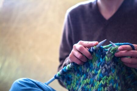 A woman knits from thick yarn. Handmade clothes. The girl sits on the couch and goes in for her hobbies. Knitting close up.の写真素材
